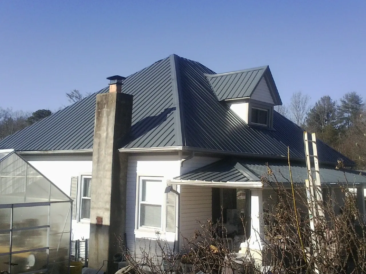 Dark blue standing seam metal roof on a white farmhouse with dormer — Slate & Tile Roof Repair by Roofing Brothers in New Virginia