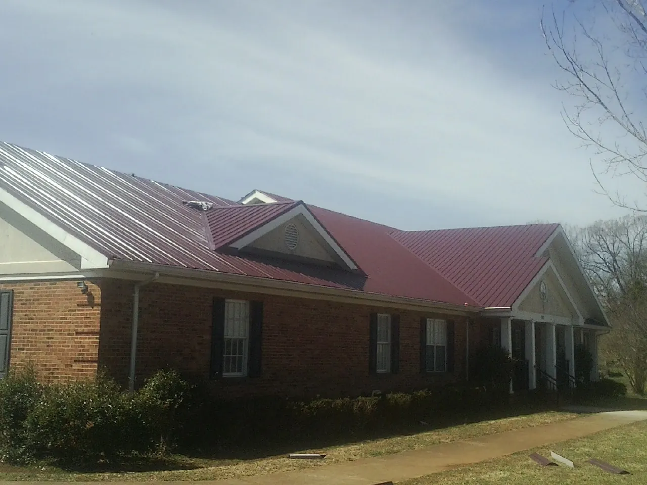 Red metal roof with gabled entries on a long brick building, from a Hail Damage Roof Repair job in New Virginia