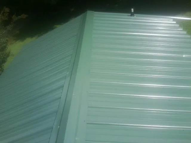 New green metal panels meeting at the ridge of a roof — Flat Roof Repair work by our crew in New Virginia
