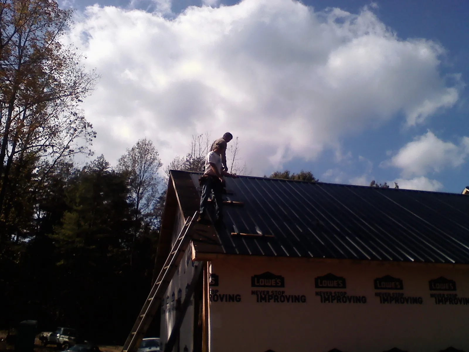 Roofer fastening dark metal panels high against a cloudy sky, from a Roof Inspection job in New Virginia