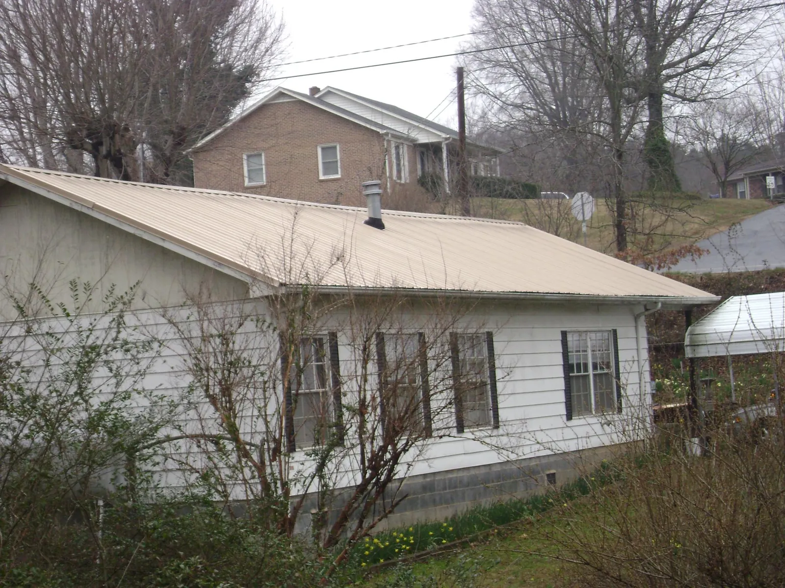Tan metal roof on a white sided house set into a hillside — Commercial Roofing by Roofing Brothers in New Virginia