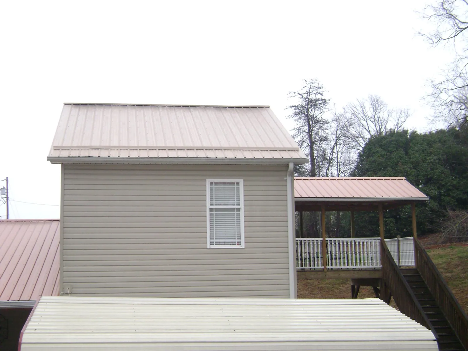Tan metal roofs on a two story addition and attached porch, from a Roof Replacement job in New Virginia